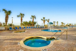 A pool area with multiple pools, lounge chairs, and palm trees. - Luxury Oceanfront 1BR | Designer Decor (North Myrtle Beach)