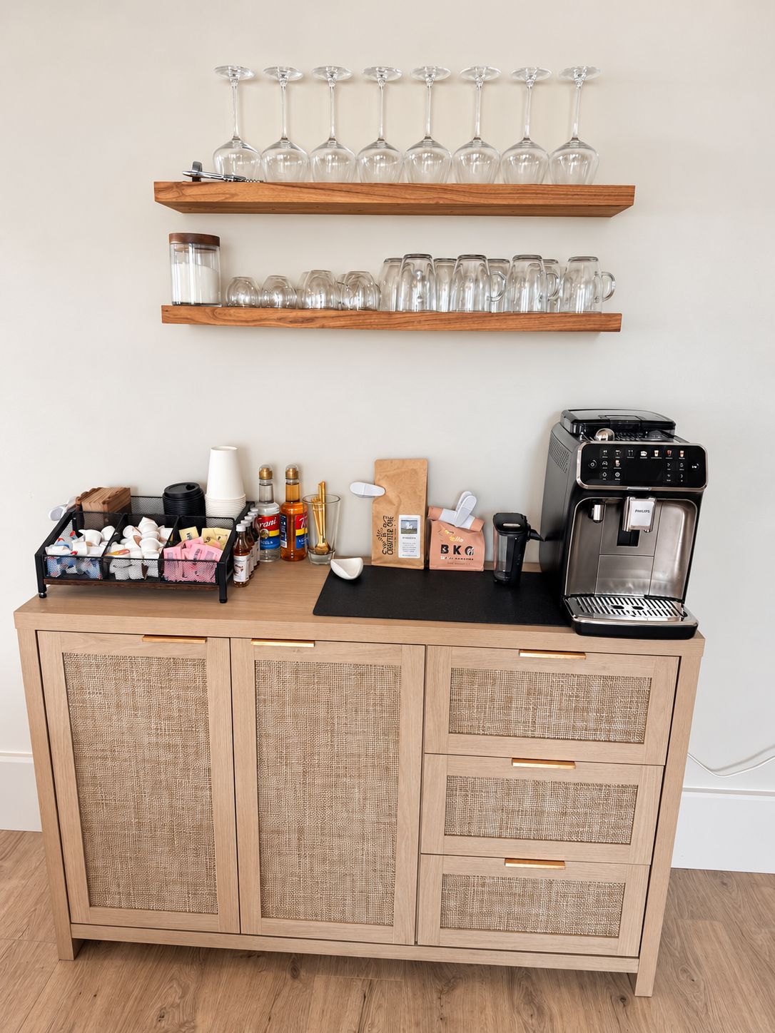 A kitchenette with a coffee machine, shelves with glasses, and storage cabinets.