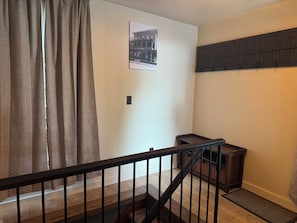 Uma escada com corrimão de madeira, um quadro pendurado na parede e uma prateleira escura.