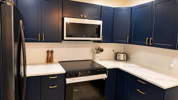 Une cuisine avec des meubles de couleur bleu foncé, un réfrigérateur en acier inoxydable, un four à micro-ondes, une cuisinière et un grille-pain.
