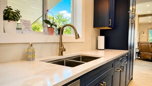 A modern kitchen with a double sink, dark cabinetry, and a window with a view.