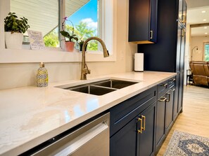 A modern kitchen with a double sink, dark cabinetry, and a window with a view.