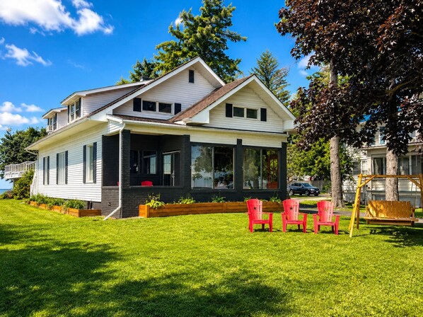 A two-story house with a covered porch, a lawn, and red chairs.