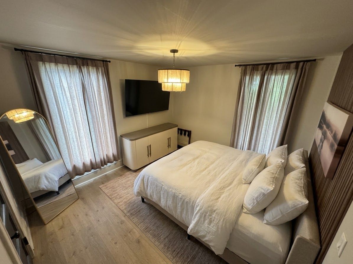 A bedroom with a bed, a flat-screen TV, a bedside table, and a mirror.