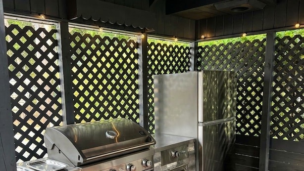 An outdoor kitchen area with a grill, a refrigerator, and a stone countertop.