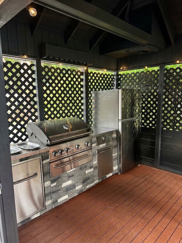 An outdoor kitchen area with a grill, a refrigerator, and a stone countertop.