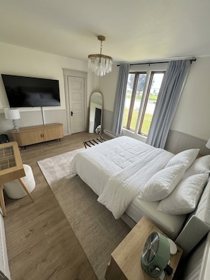 Quarto com cama grande, televisão, espelho e janela com cortinas.