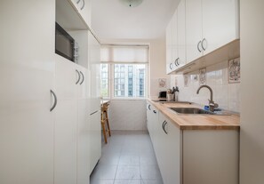A narrow kitchen with white cabinets, a wooden countertop, and a window providing a view of buildings outside. - Warsaw Royal Route Apartment (Warszawa)