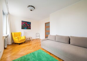 A living room with a sofa, a yellow armchair, a green rug, a radiator, and a painting on the wall. - Warsaw Royal Route Apartment (Warszawa)