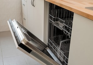 An open dishwasher with a stainless steel finish, a wooden countertop above, and a tiled backsplash. - Warsaw Royal Route Apartment (Warszawa)