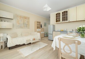 A modern kitchen with white cabinets, a dining table set for two, and a cozy living area with a fluffy white sofa. - Dunikowskiego Cosy Apartment (Szczecin)
