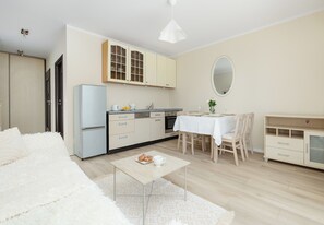 A modern kitchen with a refrigerator, cabinets, and a dining area with a table and chairs. - Dunikowskiego Cosy Apartment (Szczecin)