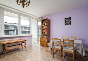 A room with a wooden table, chairs, a bookshelf, and a window with a view of buildings. - Złota Spacious Apartment (Warszawa)
