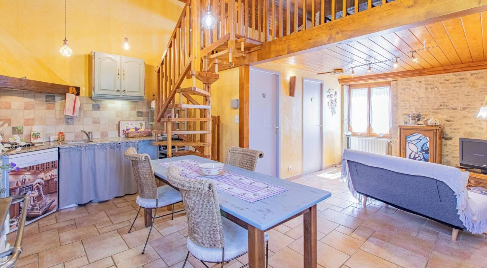 A cozy interior with a dining area, kitchen, and living space, featuring a wooden staircase and tiled floors.