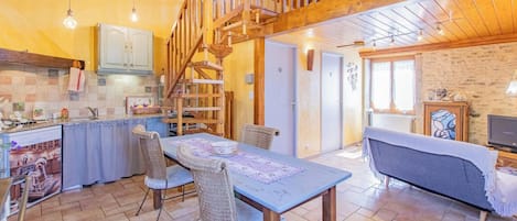 A cozy interior with a dining area, kitchen, and living space, featuring a wooden staircase and tiled floors.