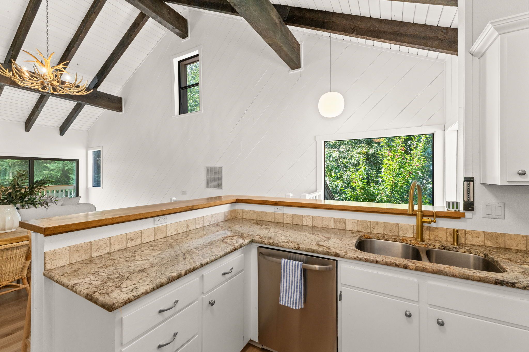 A kitchen with white cabinetry, a granite countertop, a stainless steel sink, and a built-in dishwasher.