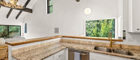 A kitchen with white cabinetry, a granite countertop, a stainless steel sink, and a built-in dishwasher.