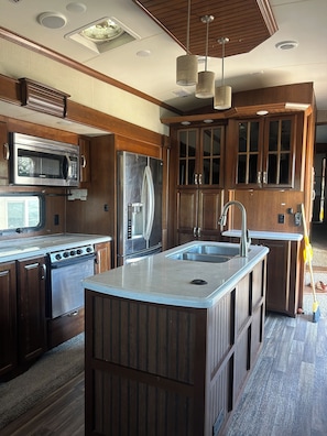 A modern kitchen with a central island, stainless steel appliances, wooden cabinetry, and pendant lighting. - Spacious, fully stocked RV in quiet, peaceful Lynndyl (Lynndyl)