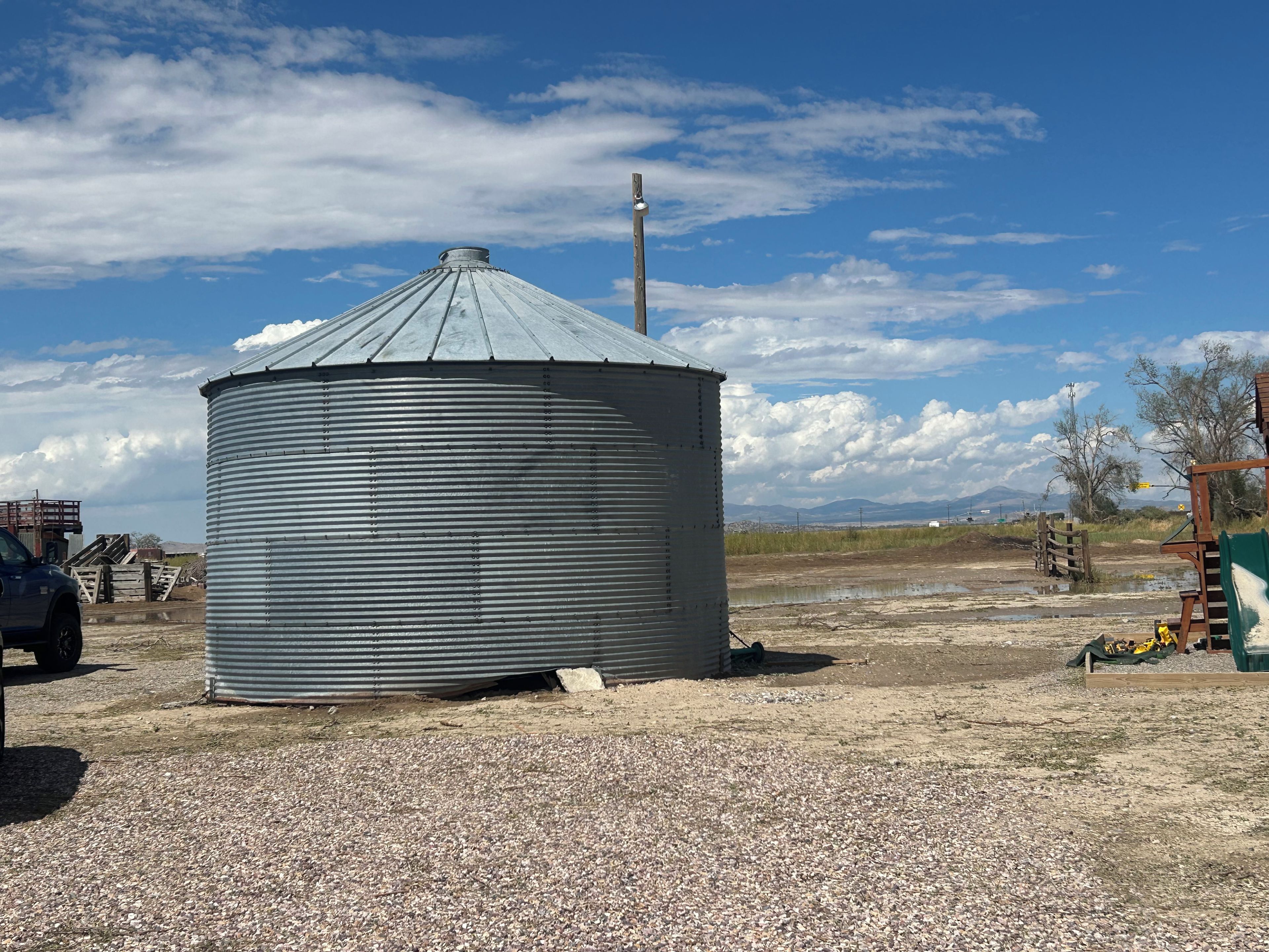 A cylindrical metal structure with a conical roof, situated on a gravel surface with a clear sky in the background.