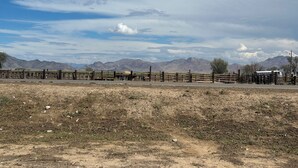 Un área cercada con suelo de tierra y montañas al fondo.