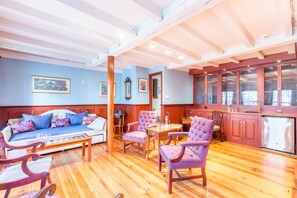 Una habitación con piso de madera, un sofá, dos sillones, una mesa de comedor y una zona de cocina con armarios y un refrigerador.