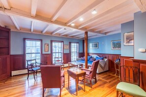 A room with a wooden floor, a sofa, a dining table with chairs, and a large window.