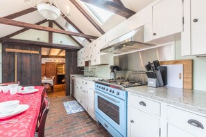 Una cocina con estufa azul, armarios blancos y una mesa roja lista para comer.