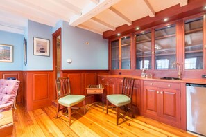 Una habitación con piso de madera, una mesa de comedor con sillas, una zona de cocina con armarios y un lavamanos, y un cuadro en la pared.