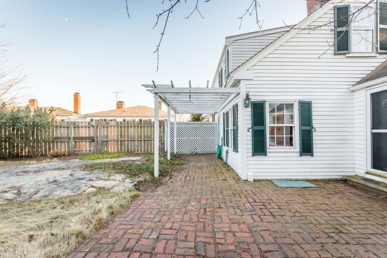 A brick pathway leading to a white house with green shutters and a covered porch.