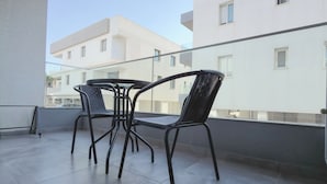 Uma varanda com mesa e cadeiras, guarda-corpo e vista para edifícios próximos.