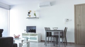 Uma sala de estar moderna com televisão de tela plana, uma mesa de jantar com cadeiras, um armário branco e uma porta de madeira.