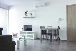 Een moderne woonkamer met een flatscreen-tv, een eettafel met stoelen, een wit kastje en een houten deur.