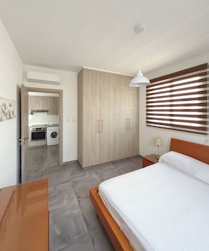 Een slaapkamer met een bed, een kledingkast, een hanglamp en een raam met jaloezieën.