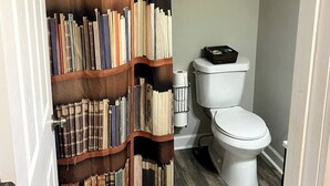 Ein Badezimmer mit einem Holzregal voller Bücher, einer weißen Toilette und einer Duschvorhang.