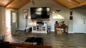 Ein geräumiges Wohnzimmer mit hoher Decke, Holzbalken, einem großen Flachbildfernseher, einem Kamin und einem Couchtisch.