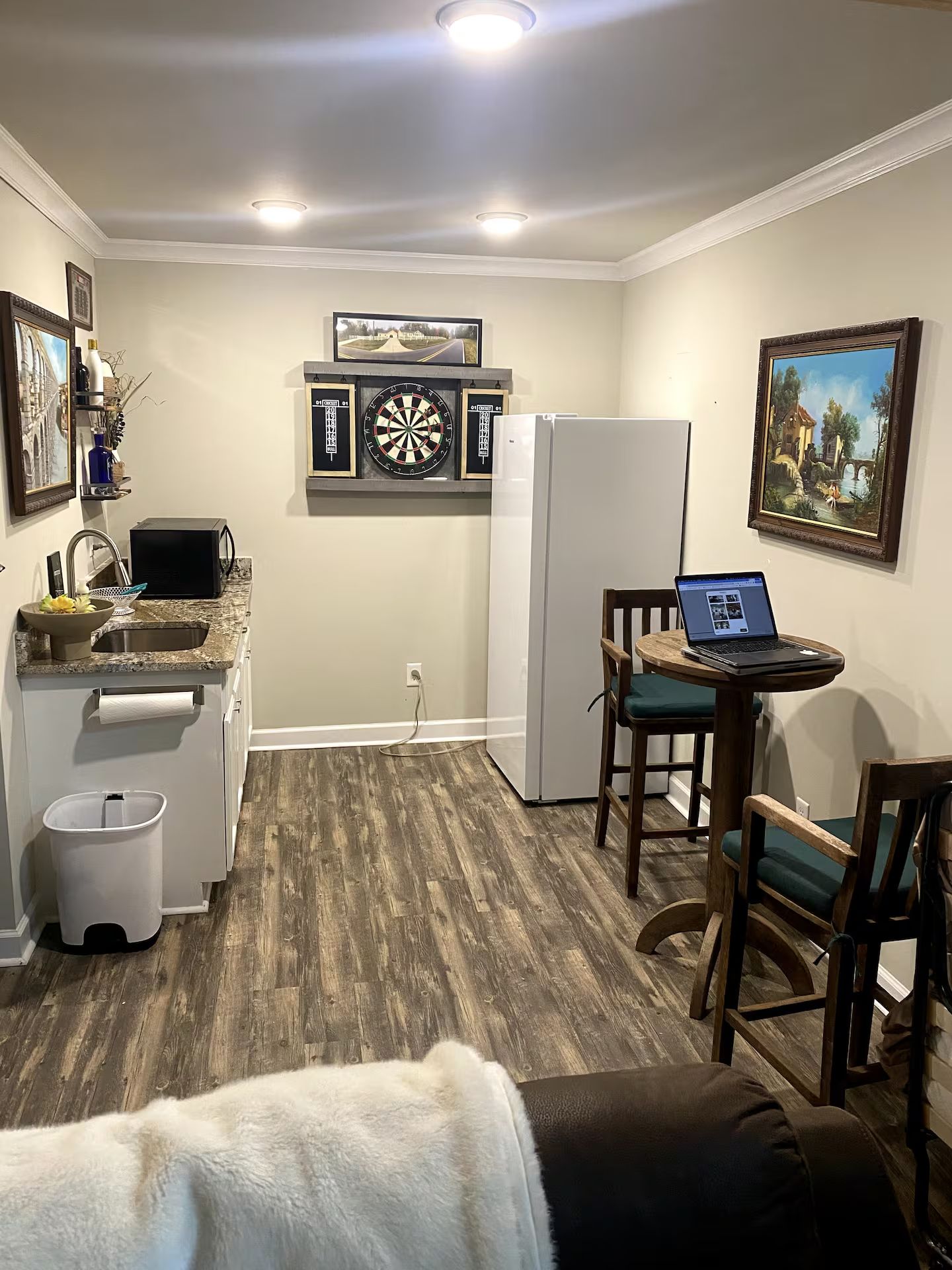 A compact kitchen with a refrigerator, microwave, and sink. There is a dining area with a laptop on a small table and two chairs.