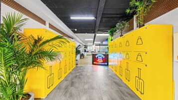 A corridor with yellow lockers, potted plants, and a sign for 'Paradise Pods' accommodation.