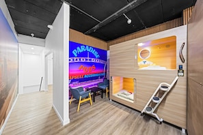 A modern interior with a wooden wall, a neon sign, a desk, chairs, and a ladder. - Sleep Different-Stay Inspired-Where inovation meets coastal living-Capsule Hotel (Benowa)