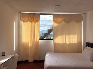 A bedroom with a bed, curtains, a desk, and a window with a view. - Comfortable Apartment Just Minutes from the UIOM Airport / Quick Access (Quito)
