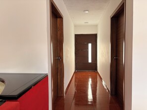 Un couloir avec une porte en bois au fond, un banc rouge sur la gauche et un sol carrelé.