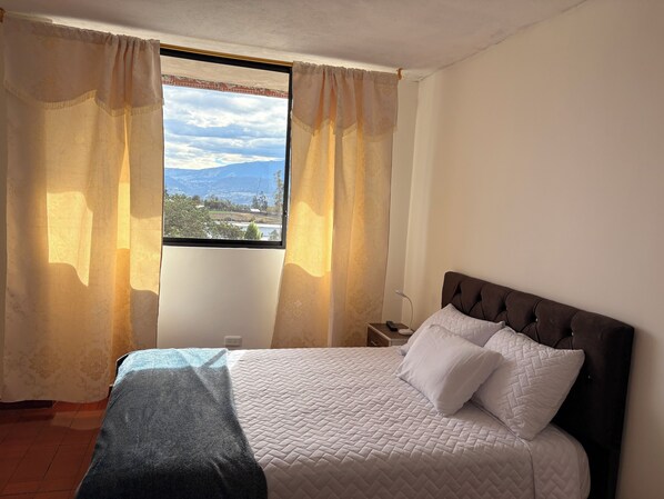 Une chambre à coucher avec un lit, des rideaux, une table de chevet et une vue sur un paysage par la fenêtre.