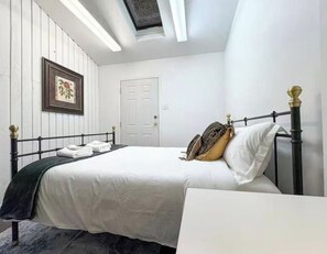 A bedroom with a bed, a bedside table, a framed picture on the wall, and a door.