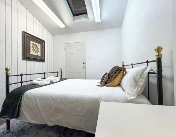 A bedroom with a bed, a bedside table, a framed picture on the wall, and a door.