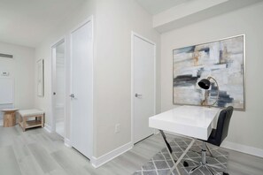 A modern room with a white desk, a chair, a large abstract painting, and a closet. - Lakeview CityPlace 2BR | Free Parking & Balcony | Parking Available (Toronto)