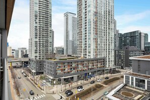 A modern urban building complex with multiple high-rise structures, a central commercial building with a glass facade, and a street with vehicles and pedestrians. - Lakeview CityPlace 2BR | Free Parking & Balcony | Parking Available (Toronto)