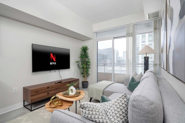 Un salon moderne avec un téléviseur à écran plat fixé au mur, un canapé, une table basse et une plante en pot.