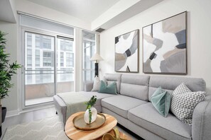 Un salon moderne avec un canapé gris, une table basse ronde en bois sur laquelle se trouve un vase blanc et une plante verte, et une œuvre d’art abstraite accrochée au mur.