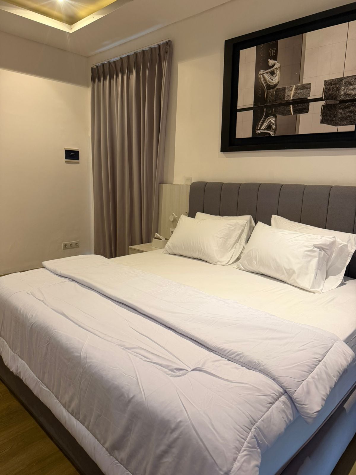 Une chambre d’hôtel avec un grand lit, une table de chevet, une lampe et une œuvre d’art encadrée au mur.
