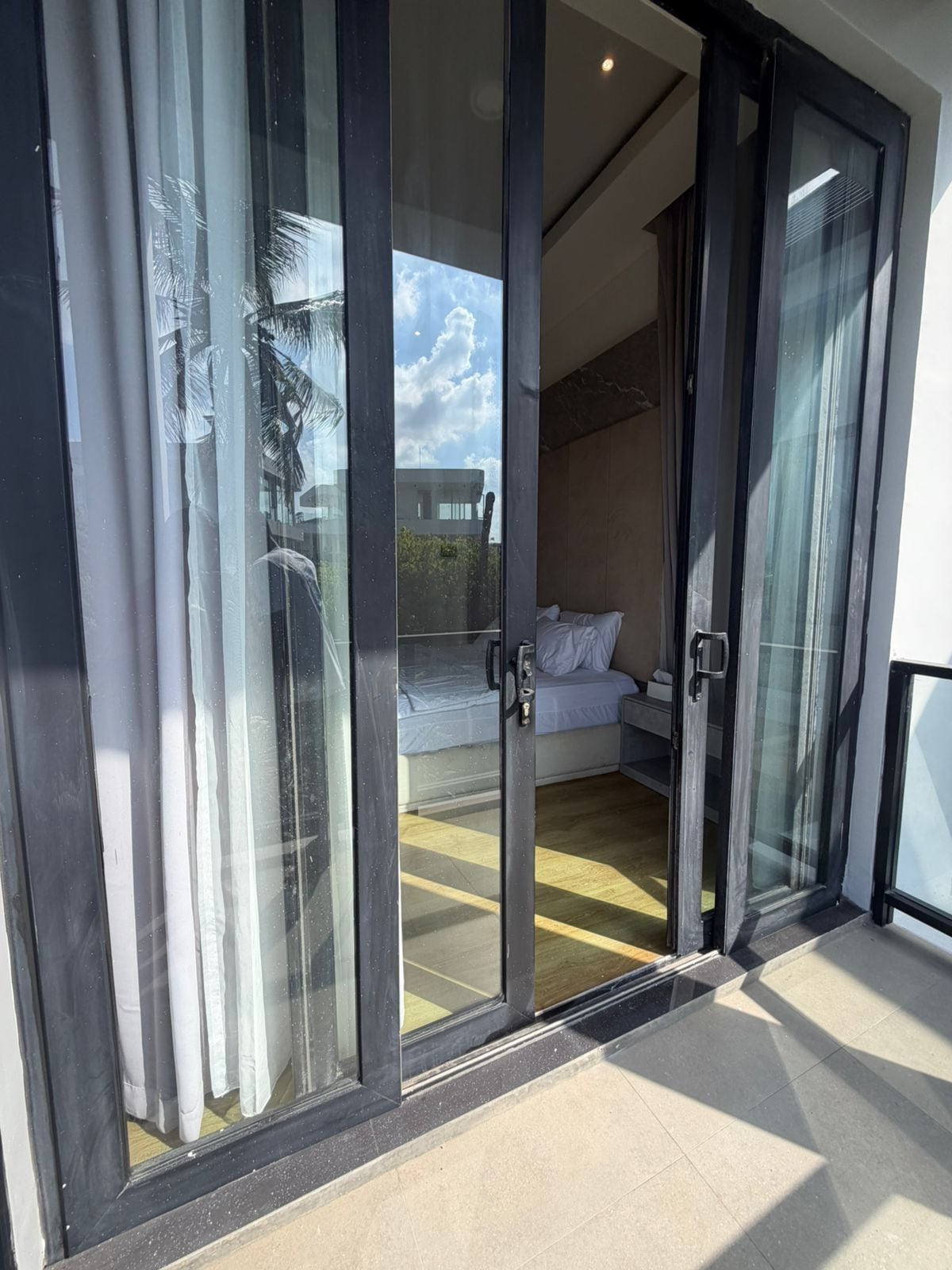 A room with a bed, a nightstand, and a view of a building through a glass door.