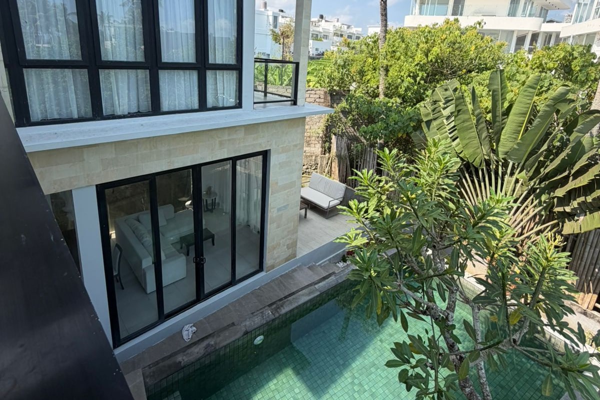 A modern two-story building with a swimming pool, outdoor seating, and lush greenery.